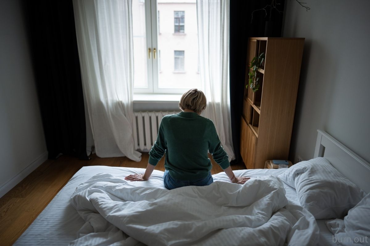 ベッドに座り窓の外を見つめる女性——休職を決断した朝のイメージ